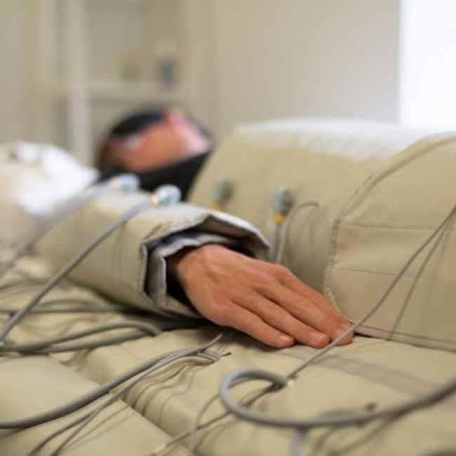 Person resting in a hospital bed with medical cables and sensors attached to their arm and chest area.